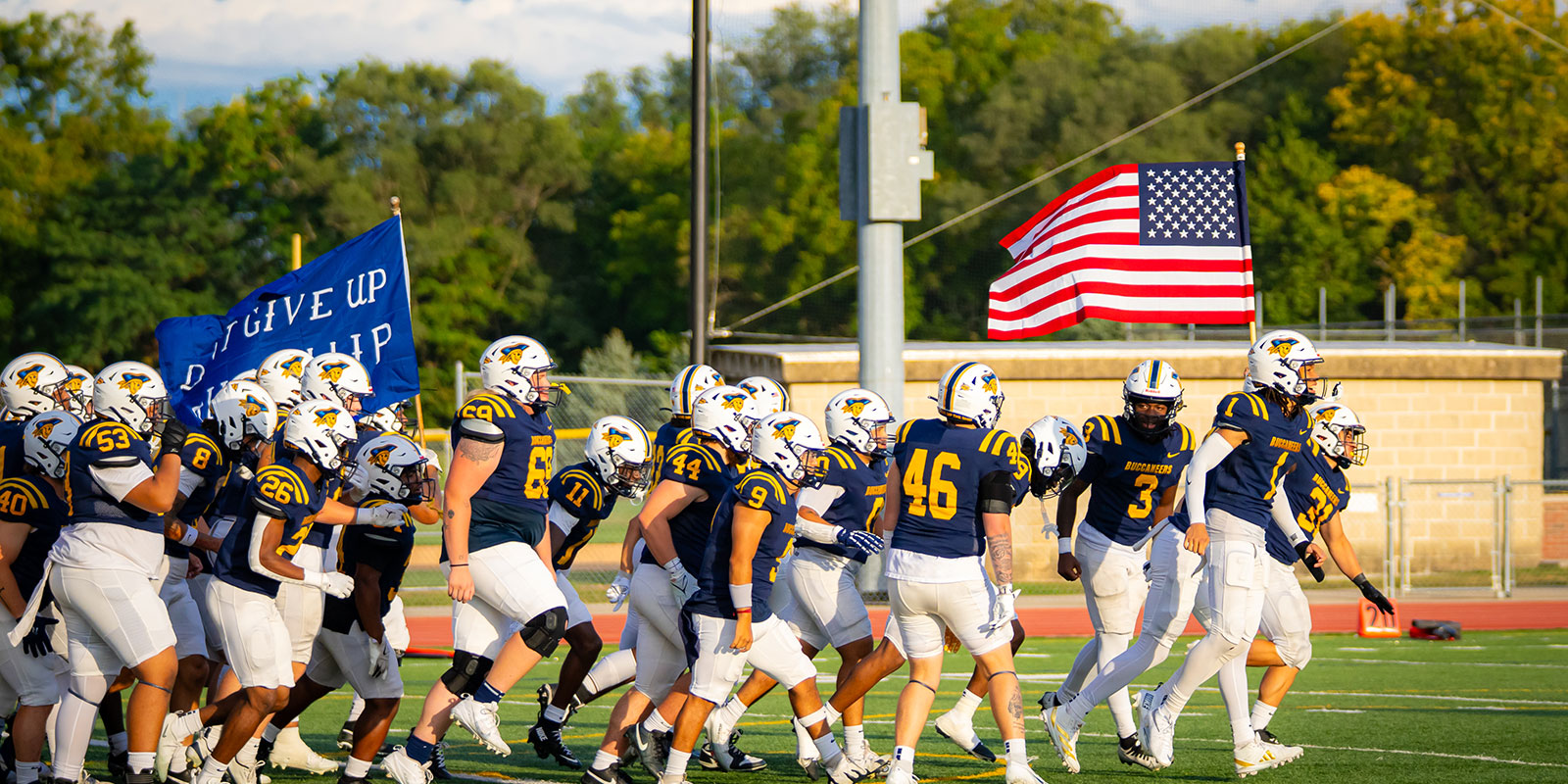 The college football team running on the field with the American flag